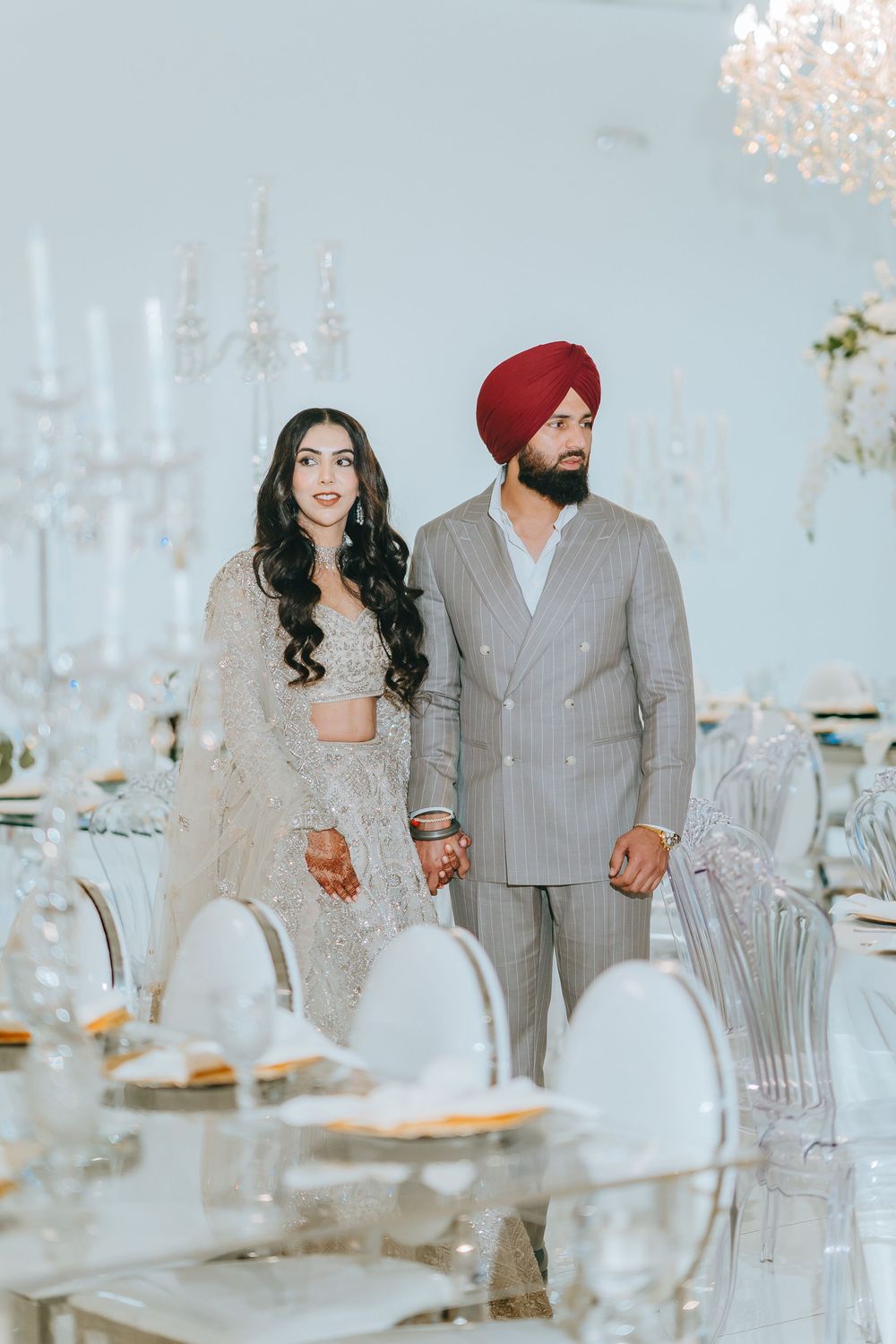 Elegant couple in traditional Indian wedding attire walking through a luxurious reception venue with crystal decor.