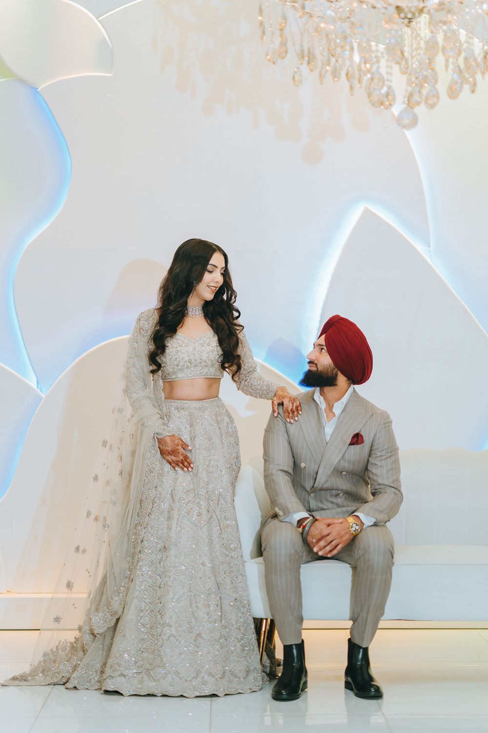Elegant wedding portraits in a modern white venue with blue lighting and crystal chandeliers overhead.