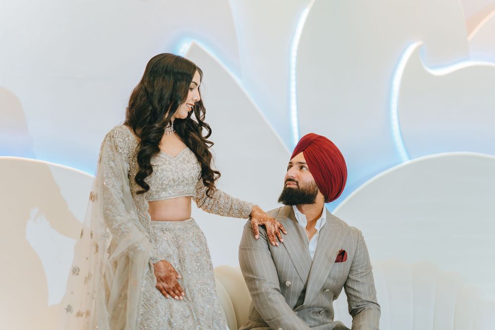 A couple in elegant Indian wedding attire poses against a modern backdrop with neon lighting.