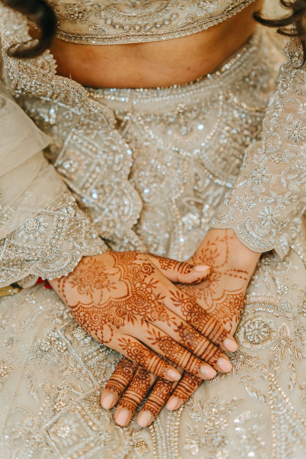 Intricate henna designs adorn hands resting on ornate white lace fabric at a traditional wedding ceremony.