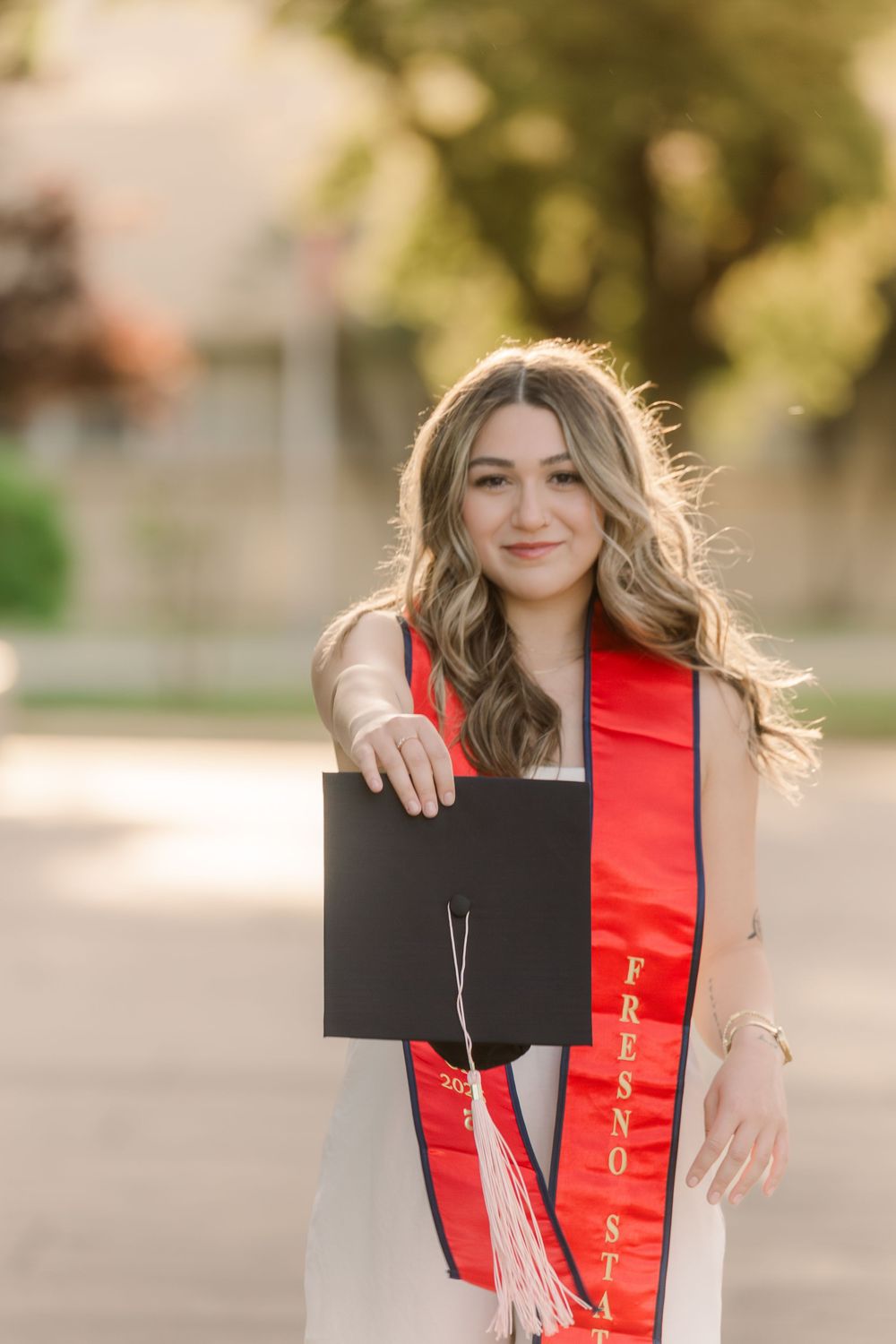 A series of graduation photos showing someone in a red stole and black gown posing outdoors on a sunny day.