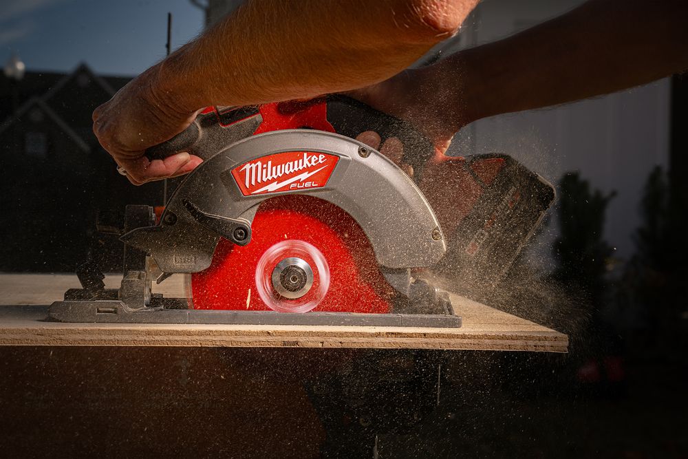 A Milwaukee circular saw with red blade cutting through wood, creating sawdust in dramatic lighting.