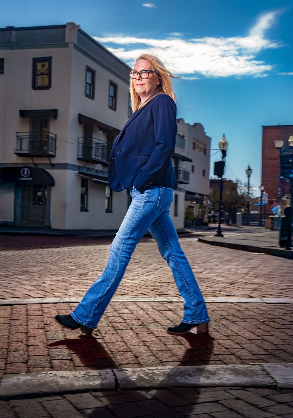 Low angle view of someone walking on brick pavement wearing blue jeans and boots against urban buildings and blue sky.