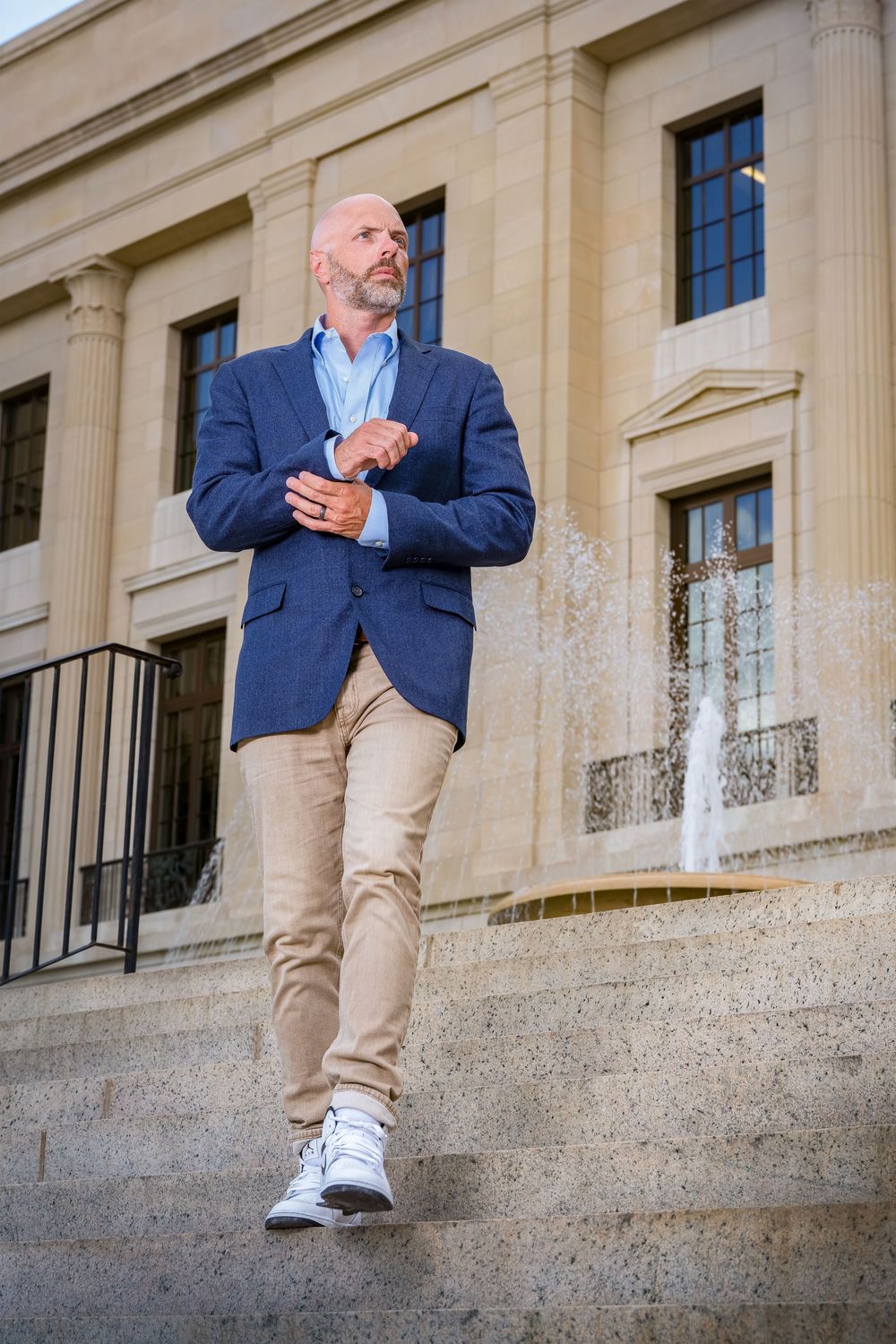 Person in a navy blazer and khaki pants sitting casually on stone steps of a classic building.