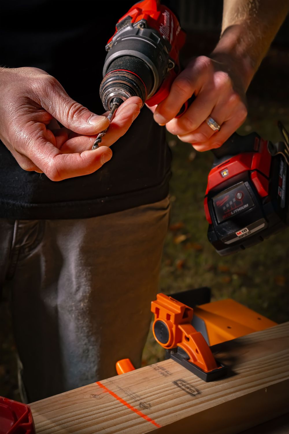 Close-up of hands using a red power drill with orange clamps and wood materials for carpentry work.
