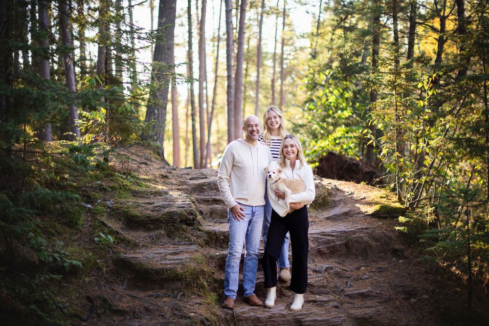 A couple walks together on a wooded forest trail during golden hour sunlight filtering through tall trees.