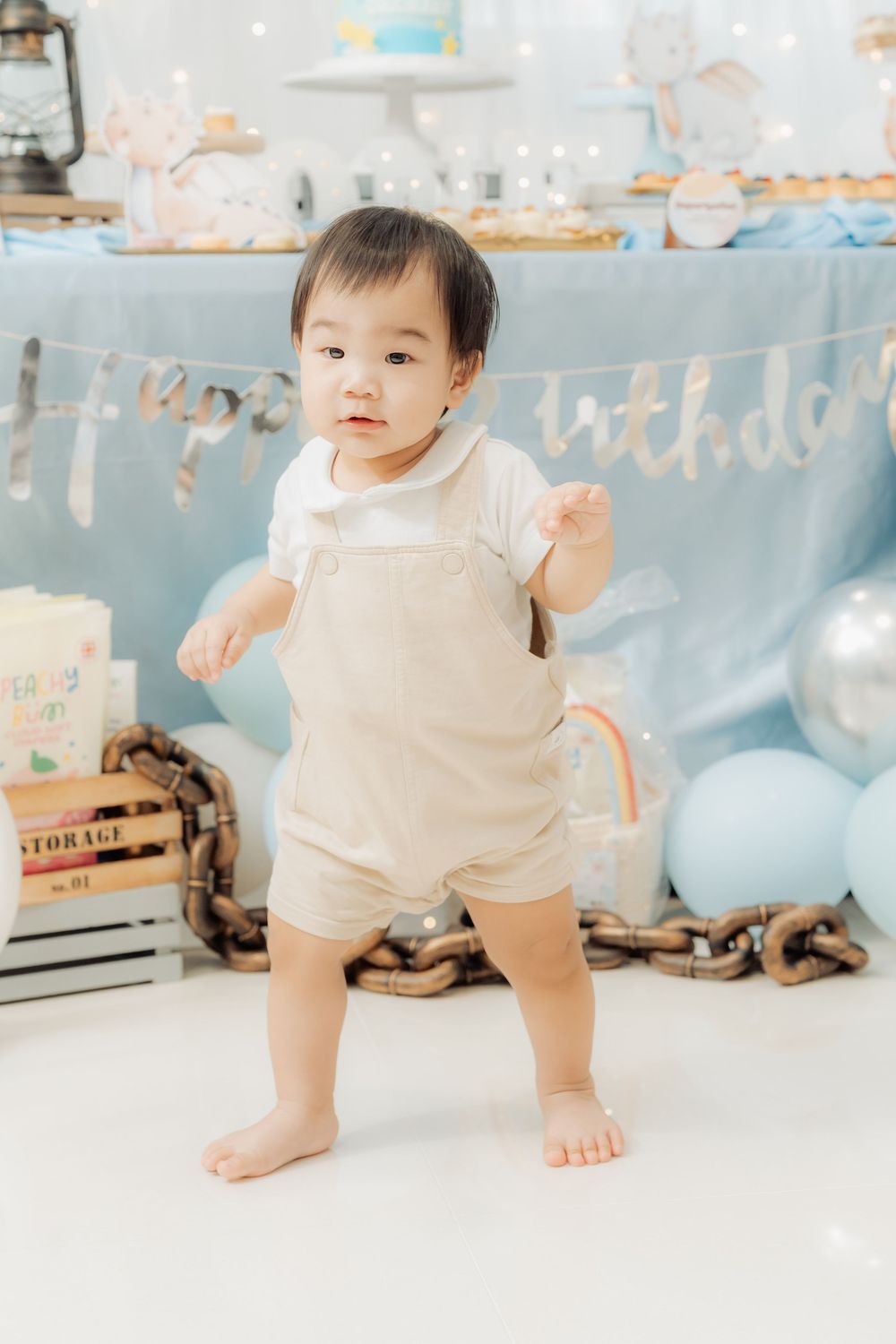 Baby in white romper crawls and plays on floor with light blue decorations in background.