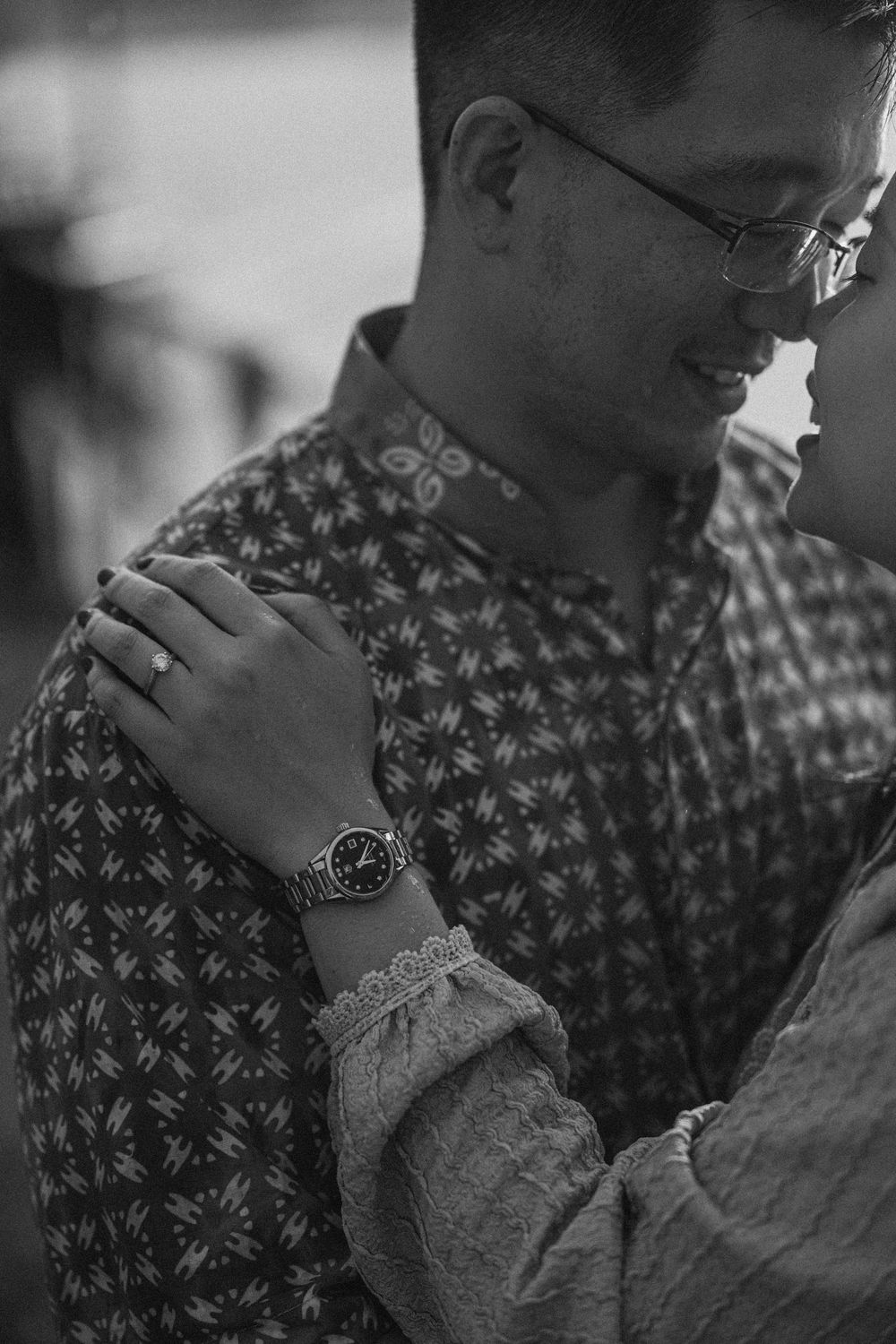 Black and white photograph showing a person wearing a patterned shirt and wristwatch in a contemplative pose.