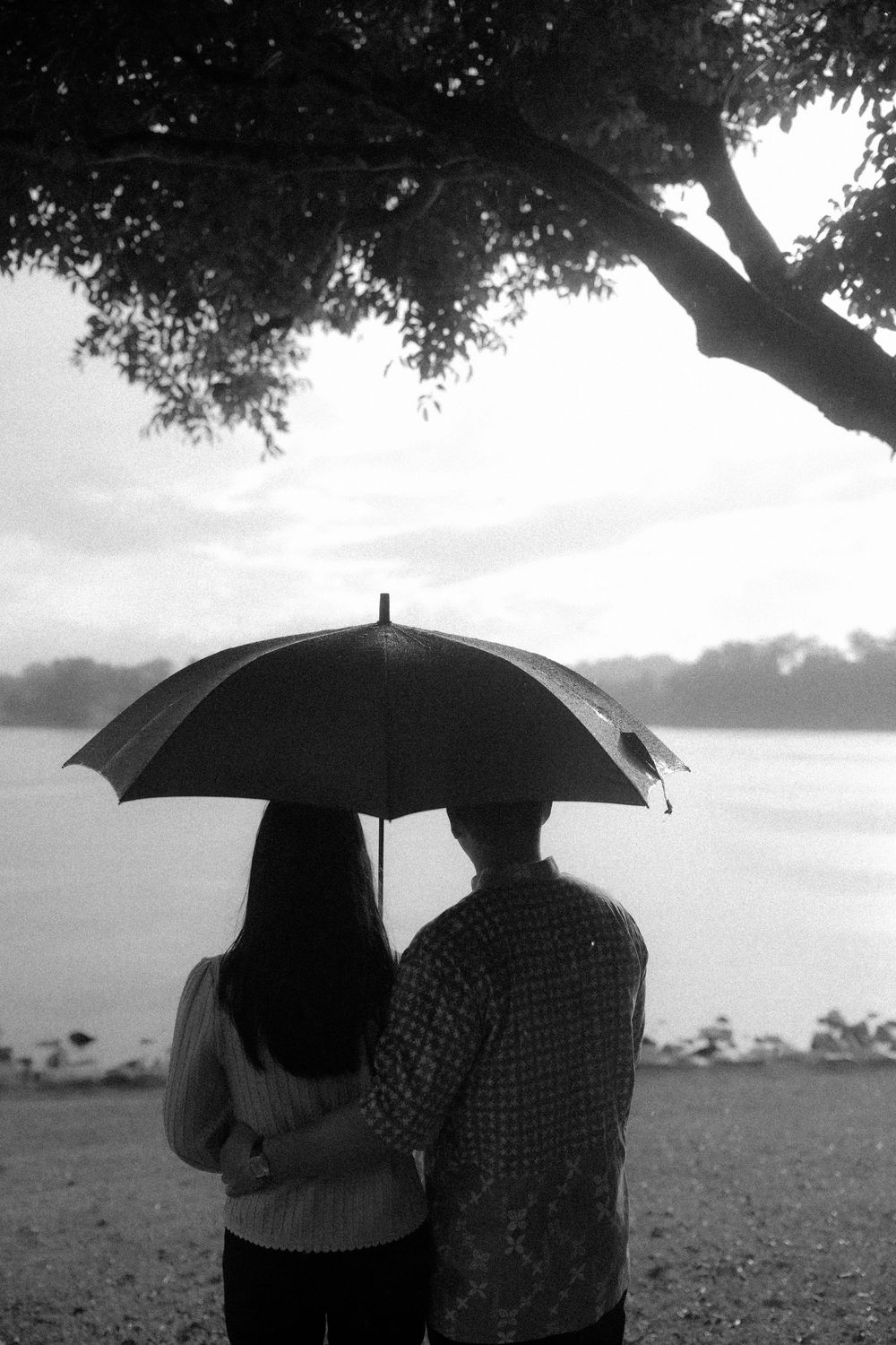 A couple shares an intimate moment under an umbrella in a black and white landscape photograph.