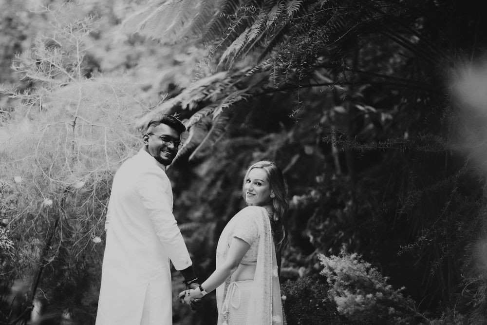 A black and white wedding photo of a couple holding hands and looking back at the camera near a rock wall.