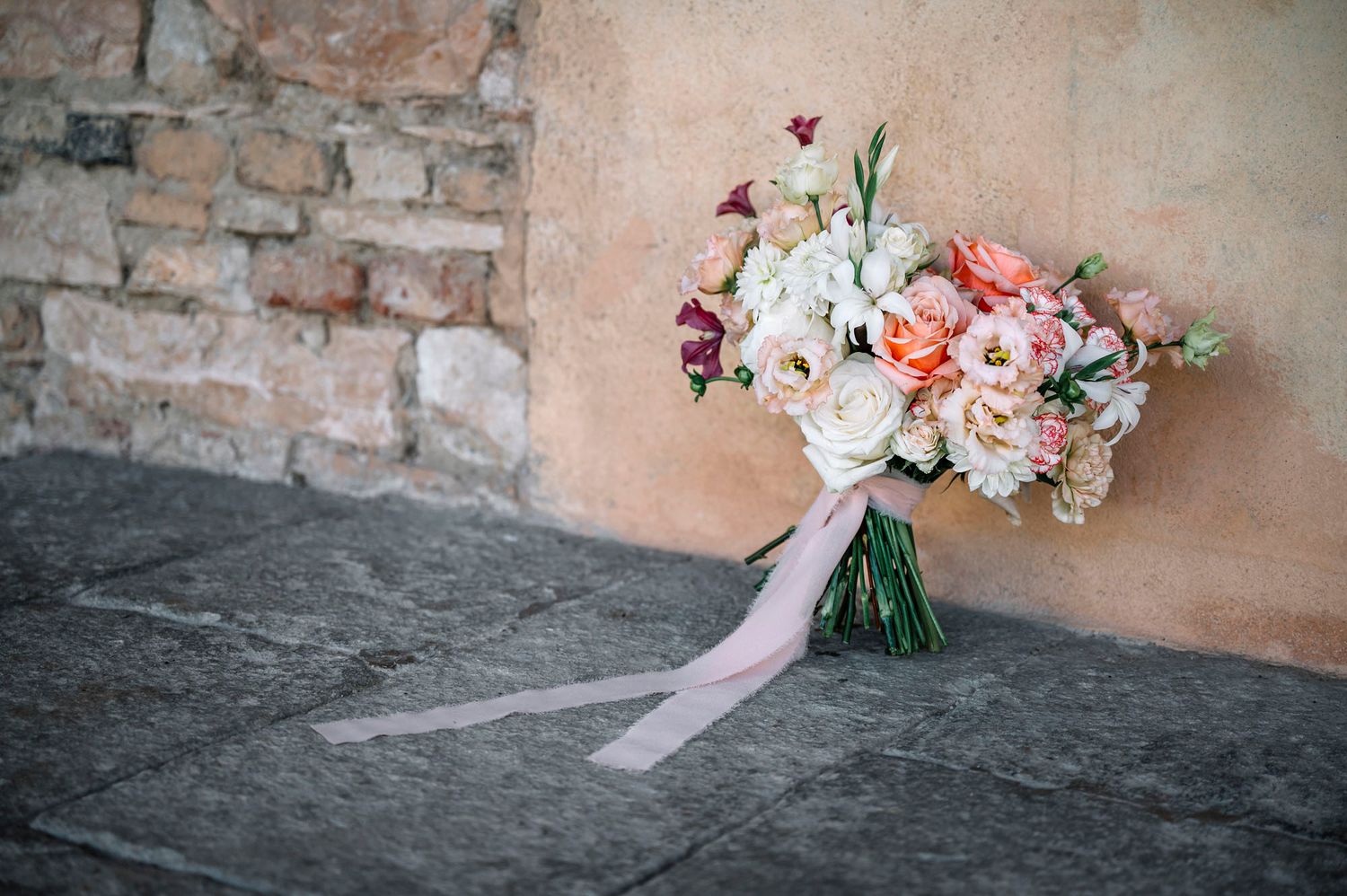 Delicato bouquet da sposa rosa e bianco appoggiato su un muro di pietra grezza.
