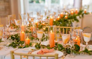 Elegant wedding reception table setting with orange candles and greenery garland centerpiece.