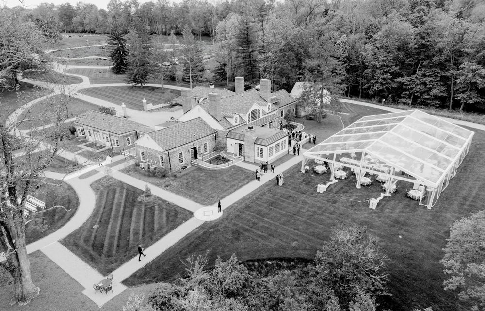 Aerial black and white photo of an elegant estate with manicured gardens and a large transparent tent.