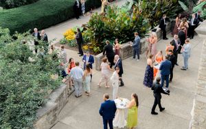 People walking and gathering in a lush garden path surrounded by green foliage and blooming flowers.