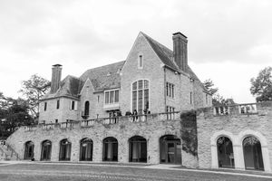 Black and white photo of an elegant stone manor house with arched windows, chimneys, and guests on the upper terrace.