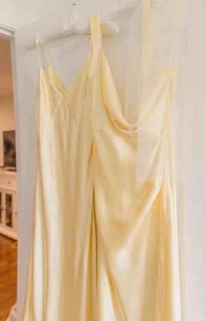 Row of pale yellow bridesmaid dresses hanging on white hangers against a light wall.