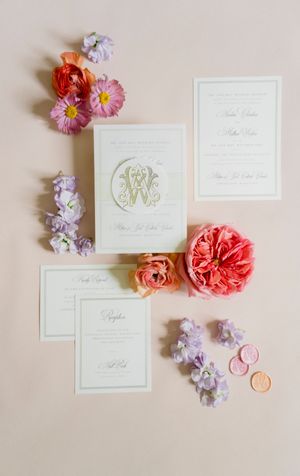 Elegant white wedding invitations decorated with pink and purple flowers arranged on a light beige background.