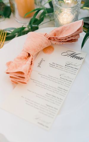 Elegant wedding menu card with pink napkin and greenery decor on white table setting.