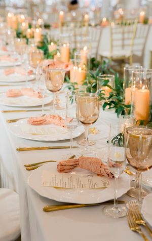Elegant wedding reception table settings with peach candles, gold flatware, and white linens.