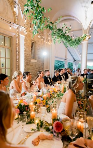 Wedding reception venue with hanging greenery, string lights, and long dining tables set for guests.