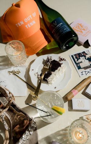 Orange baseball cap and wine bottles on table with scattered photos and candlelight.