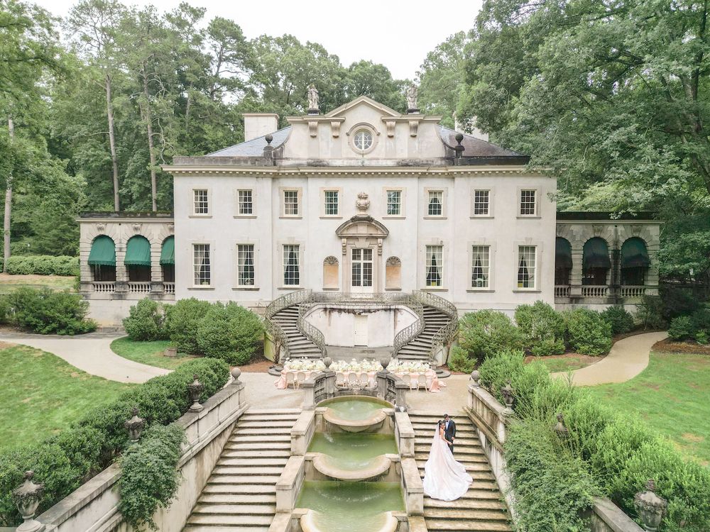 Bride poses on steps of elegant white Georgian mansion with fountain garden and lush trees in Atlanta.