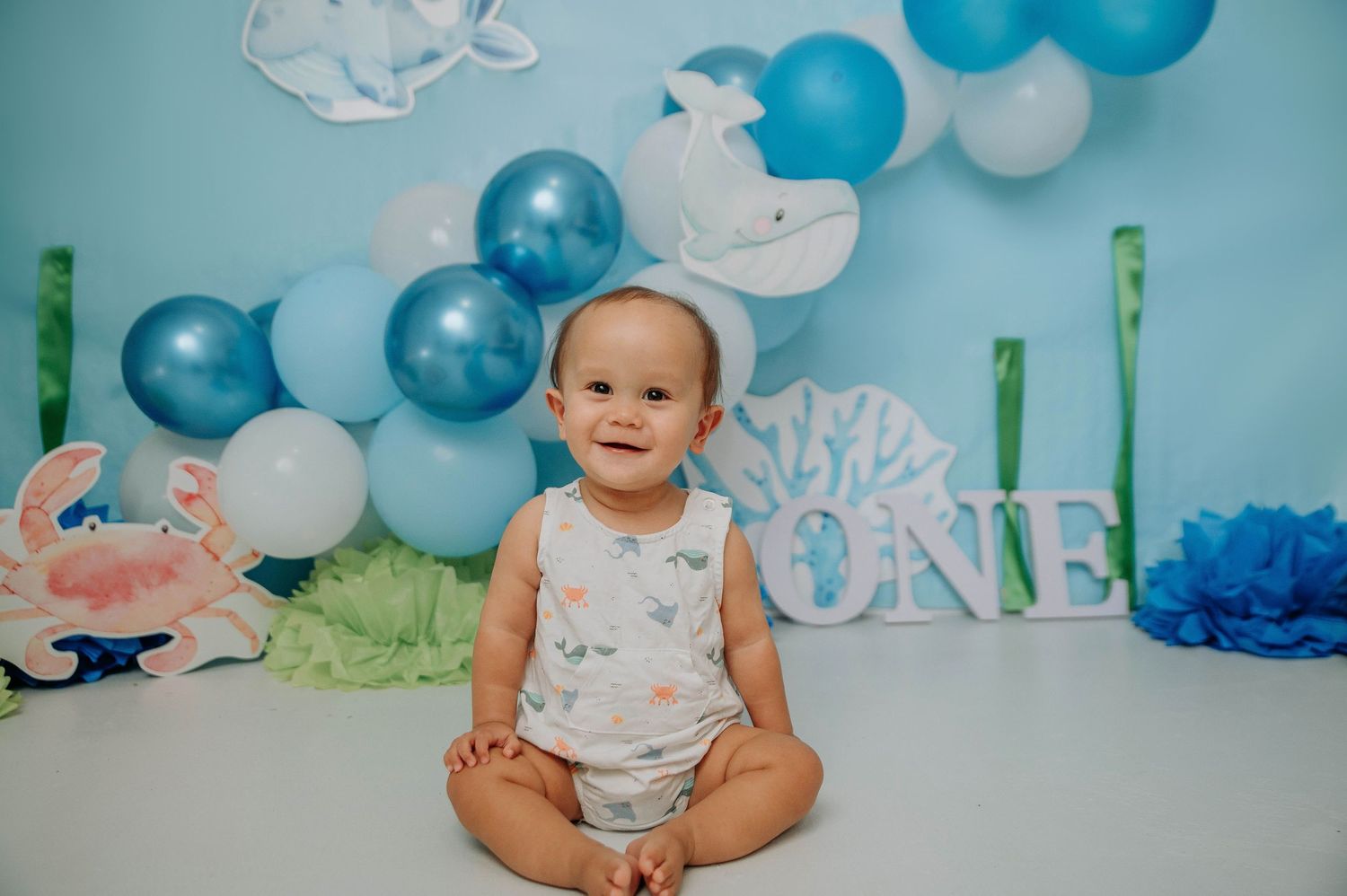 First birthday party setup with blue and white balloons, clouds and decorative elements against a light backdrop.