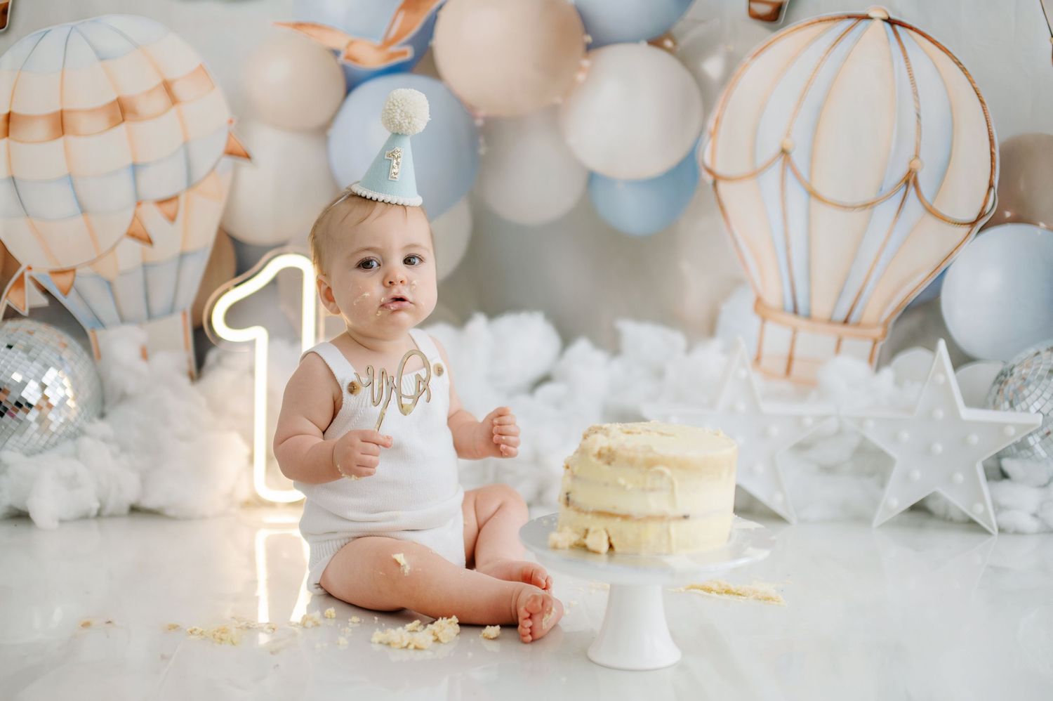 A cake smash photo collage with white and gold decorations, balloons, and a naked cake for a first birthday celebration.