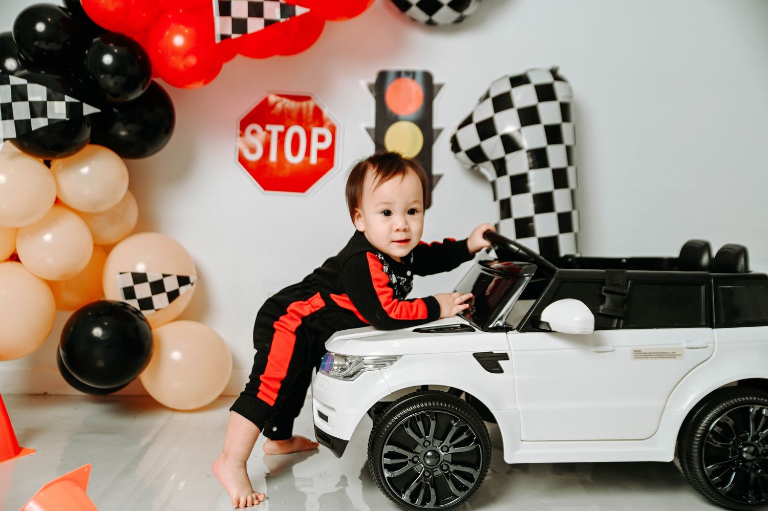 Racing-themed birthday party decorations with black and white checkered balloons, red accents, and toy cars on display.