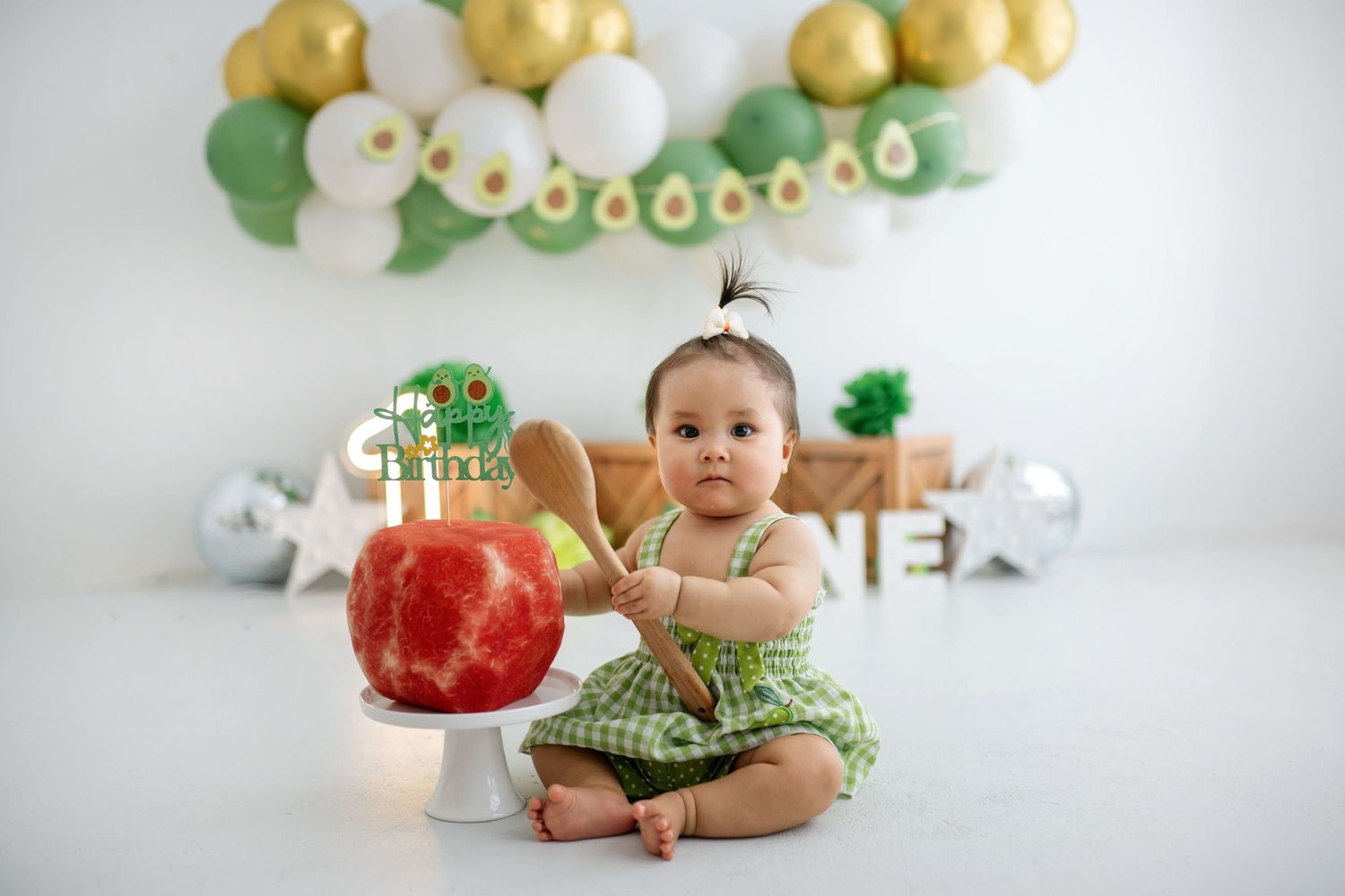 First birthday cake smash setup with gold and green balloon arch, decorative cake, and St. Patrick's Day theme.