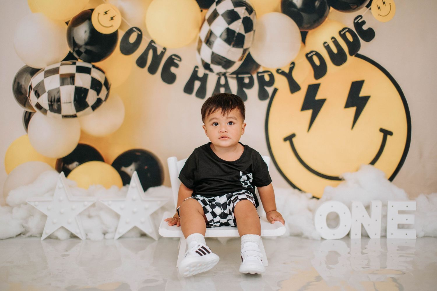 First birthday party setup with black and white checkered balloons, smiley face decor, and lightning bolt designs.