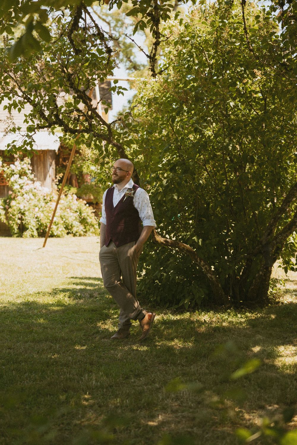 A person in casual attire walks through a sunlit orchard with green trees casting dappled shadows on the grass.