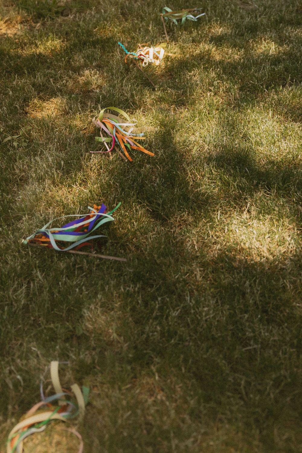 Colorful wedding ribbons and wands scattered on grass in dappled sunlight during an outdoor celebration.