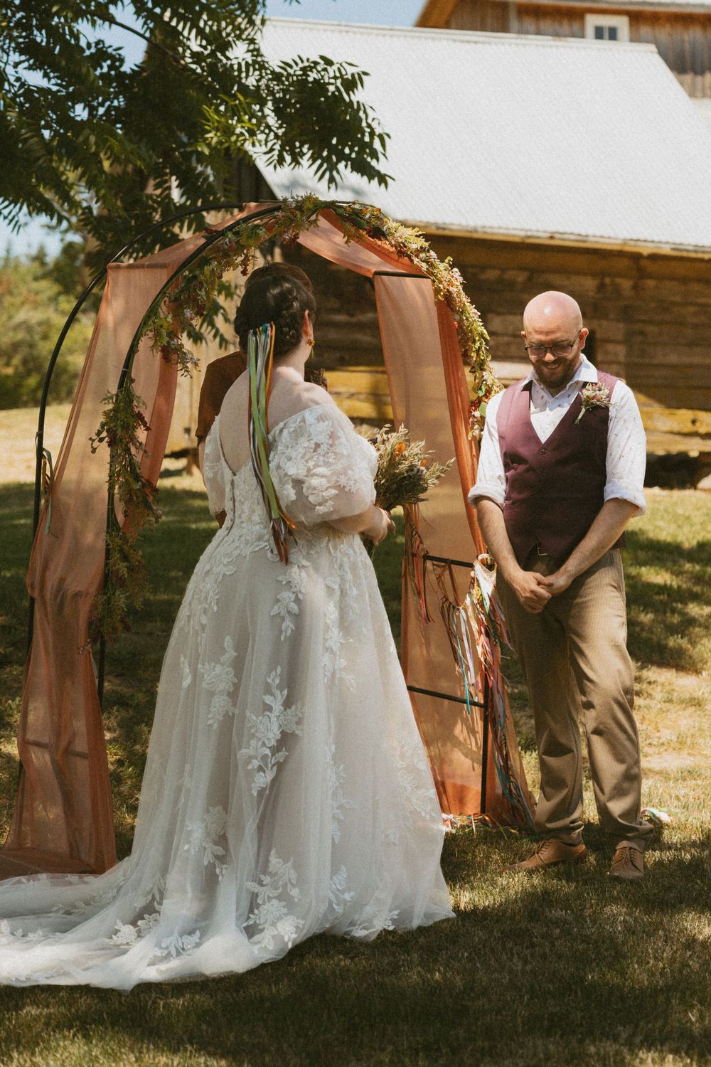 Romantic first look moment between bride and groom behind rustic wooden door in sunny outdoor garden setting.