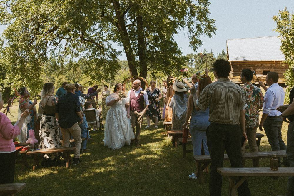 A group of people gathered outdoors for a celebration event under trees during golden hour lighting.