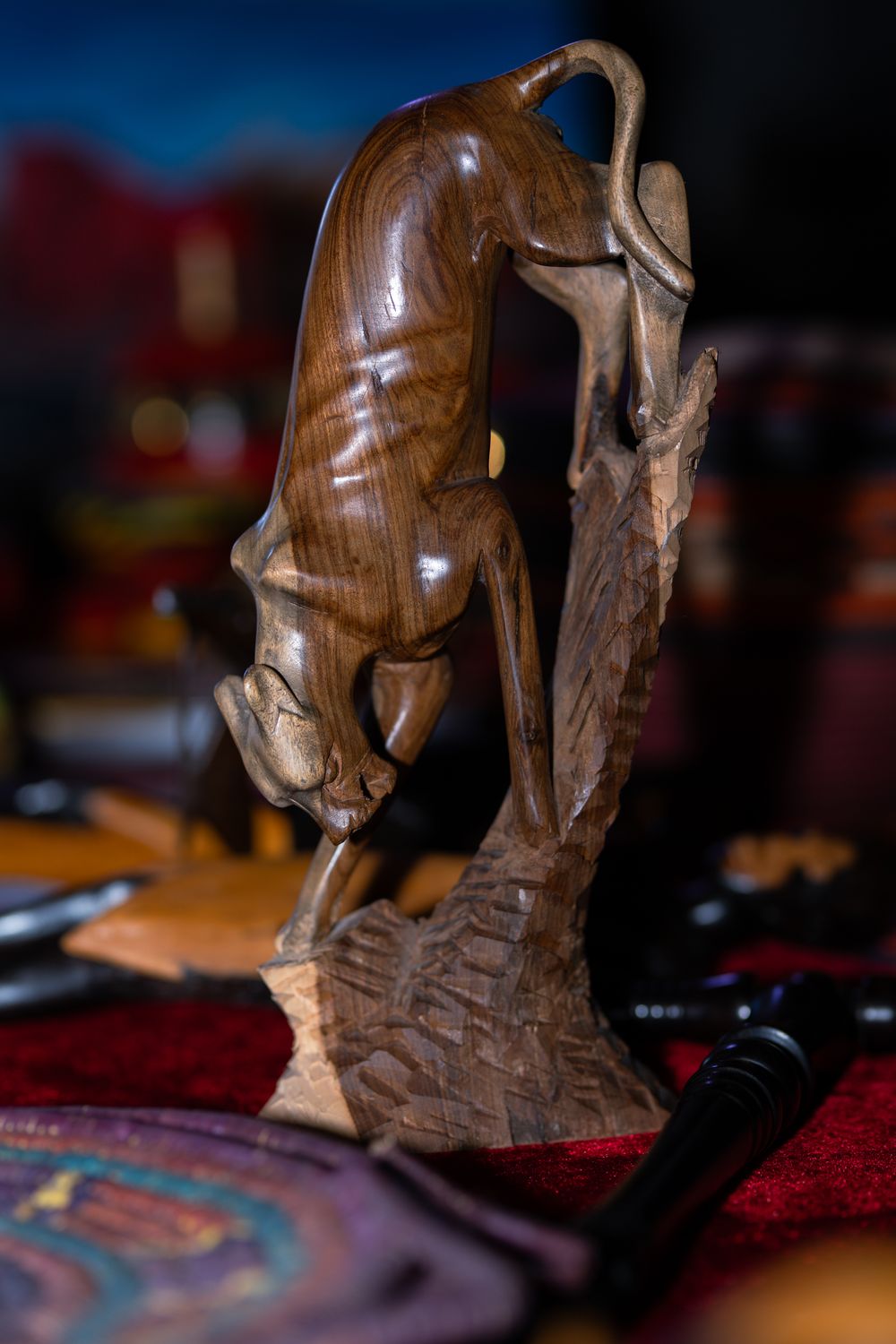 Hand-carved wooden panther sculpture descending a tree, displayed on a red velvet surface.