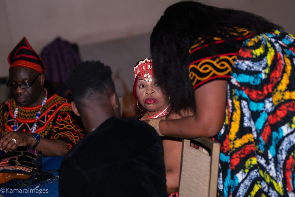 Three people in vibrant African traditional attire engage in conversation at a cultural event.
