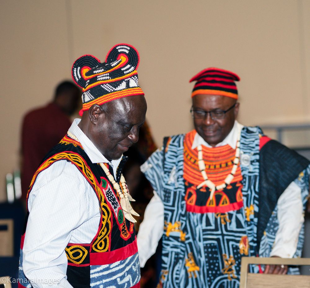 Two men in vibrant traditional African attire with colorful beaded accessories at a cultural event.