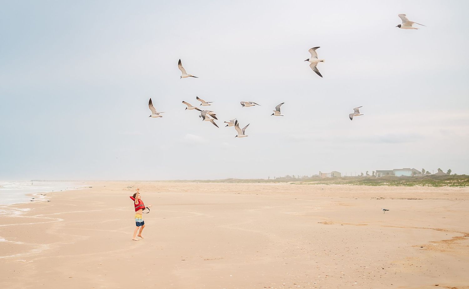Child running on a sandy beach with birds flying overhead in Matagorda, Texas on a coastal family vacation