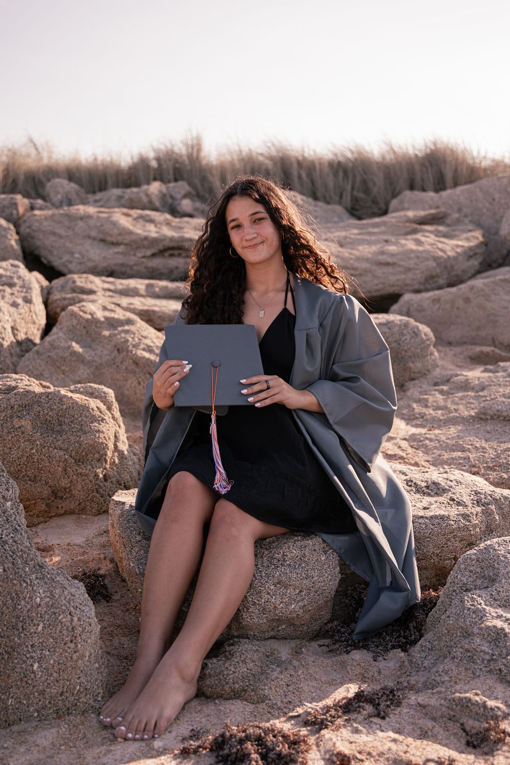 Person relaxing on rocky beach while using a tablet device in casual attire.