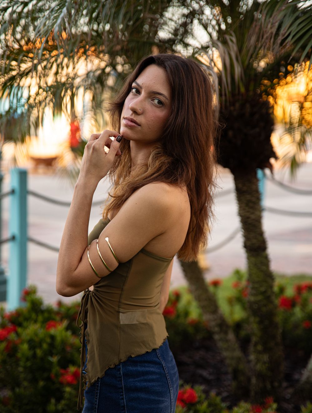 Portrait session among palm trees and flowers during sunset with warm lighting.