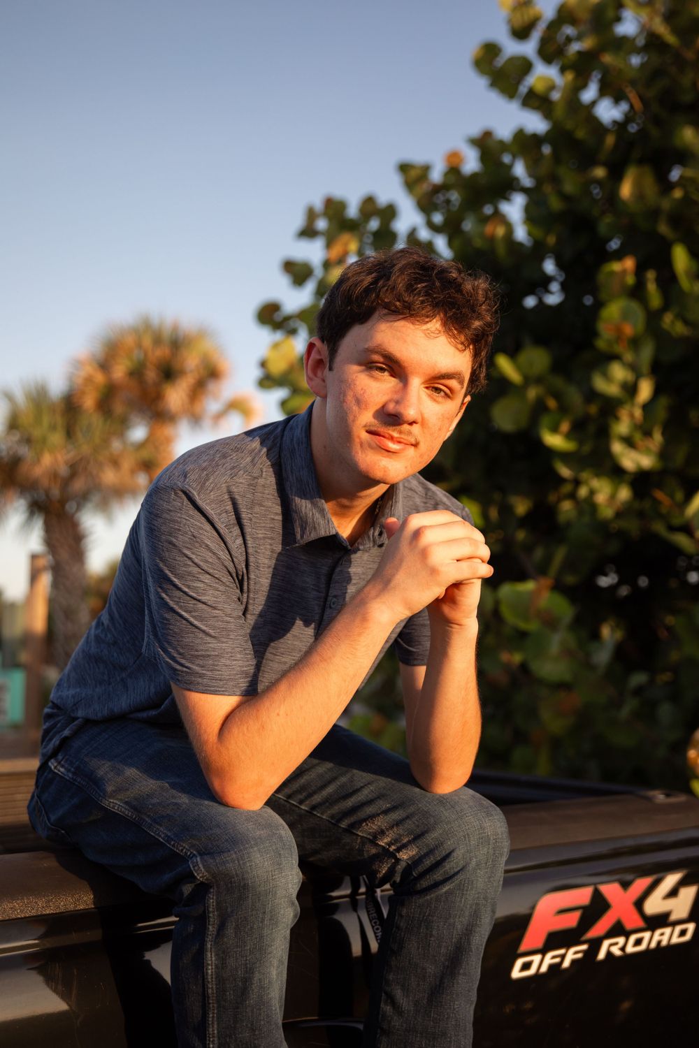 Person sitting thoughtfully on truck tailgate during golden hour.