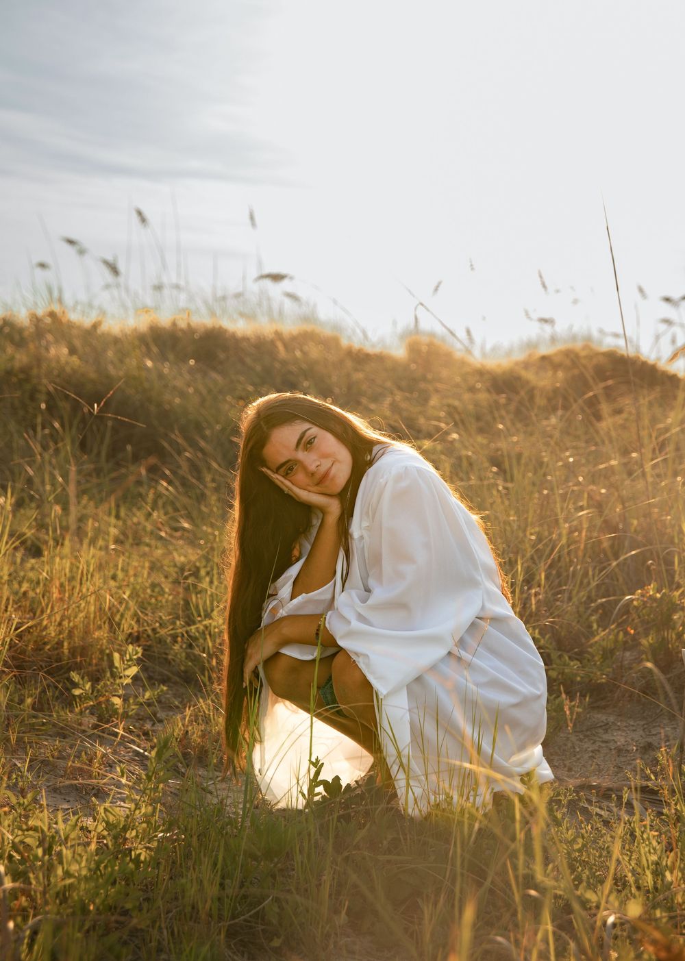 A dreamy portrait of someone in white clothing posed in tall golden grass at sunset.