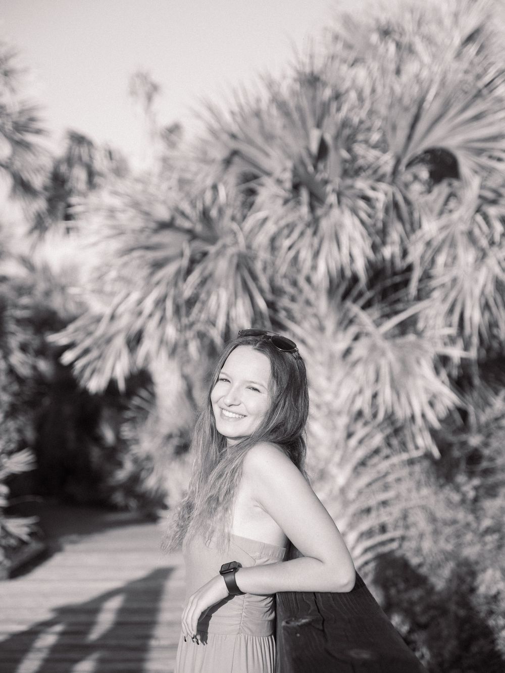 Black and white portrait of person laughing joyfully with palm trees in background.