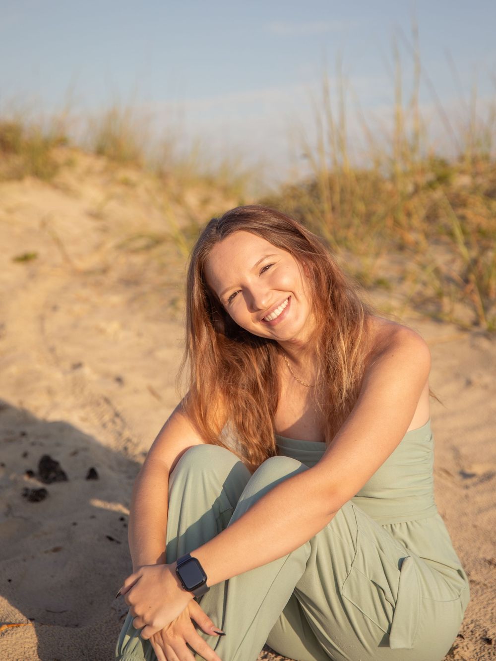 Person in green dress sitting casually on sandy dunes during golden hour.
