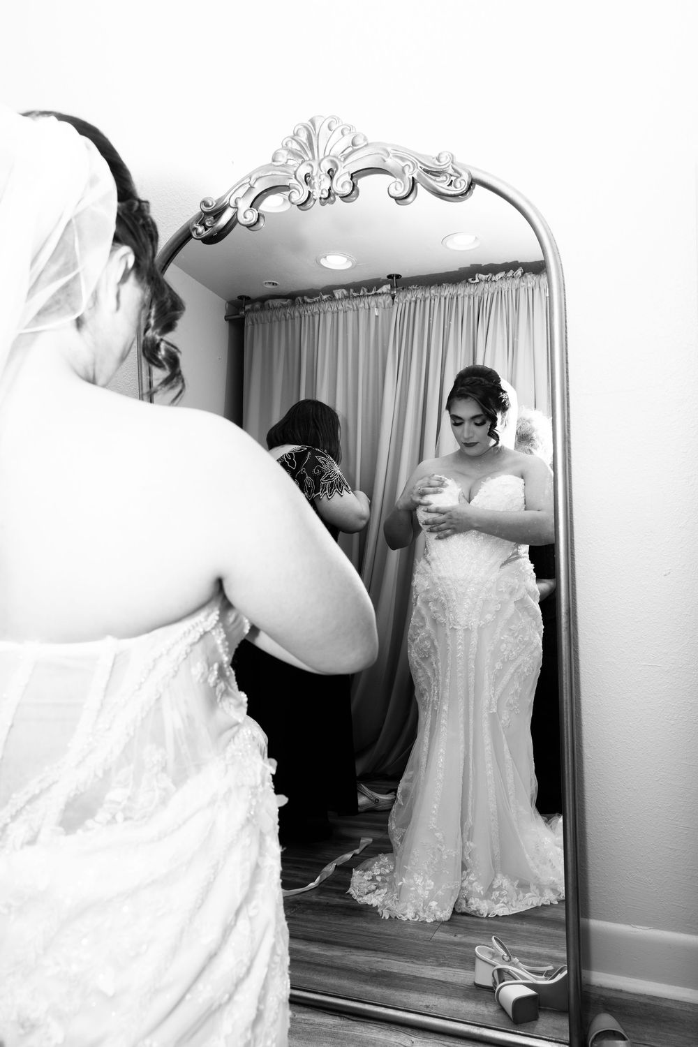 A woman in a wedding dress stands in front of a mirror, examining her reflection.