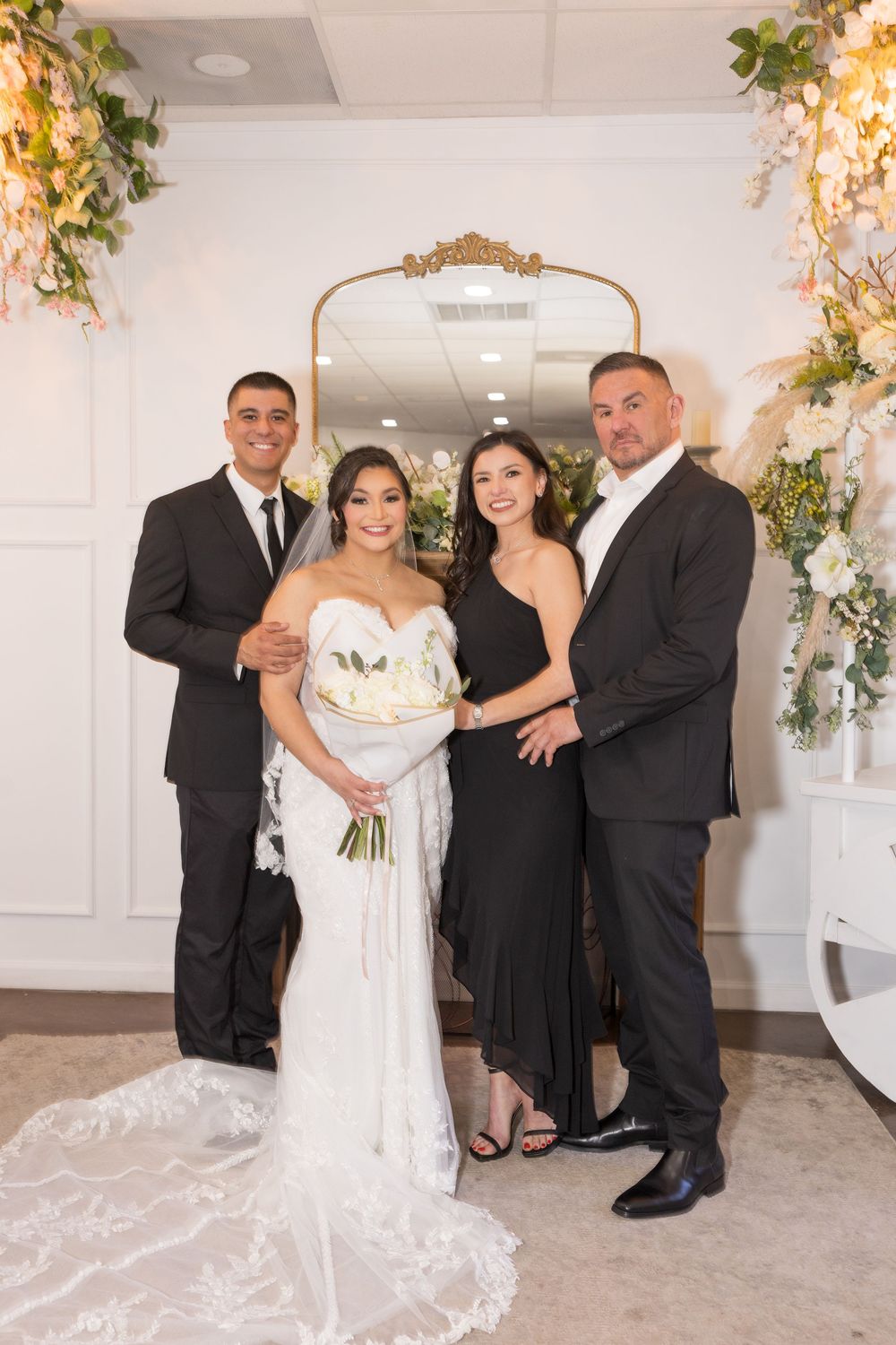 A bride and groom posing for a wedding photo with two other people in formal attire.