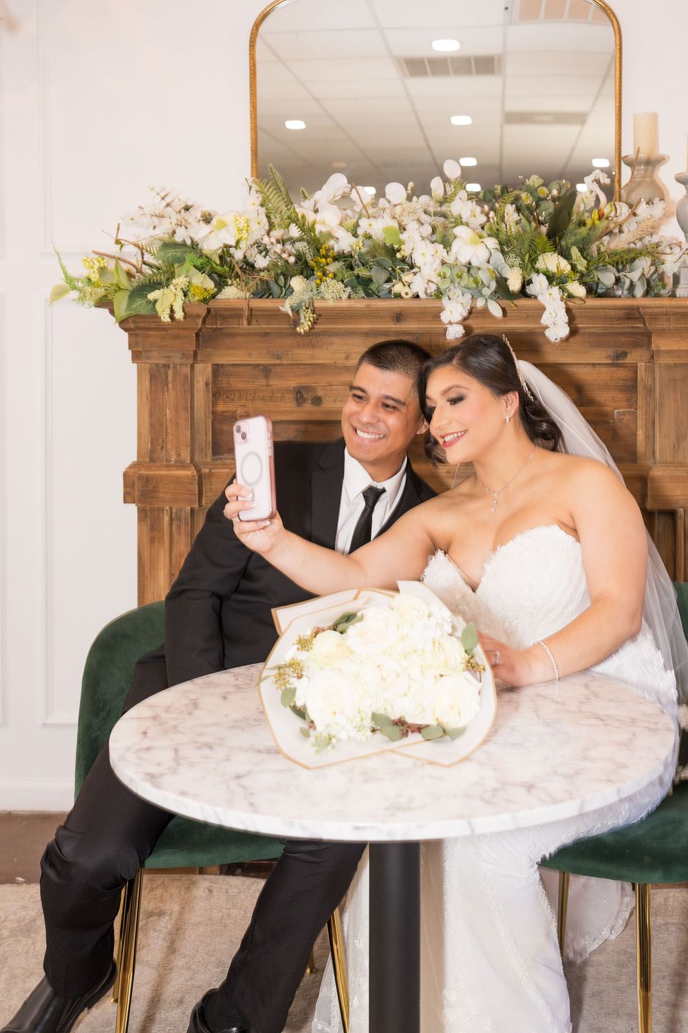 A bride and groom taking a selfie together at their wedding reception, surrounded by floral arrangements.