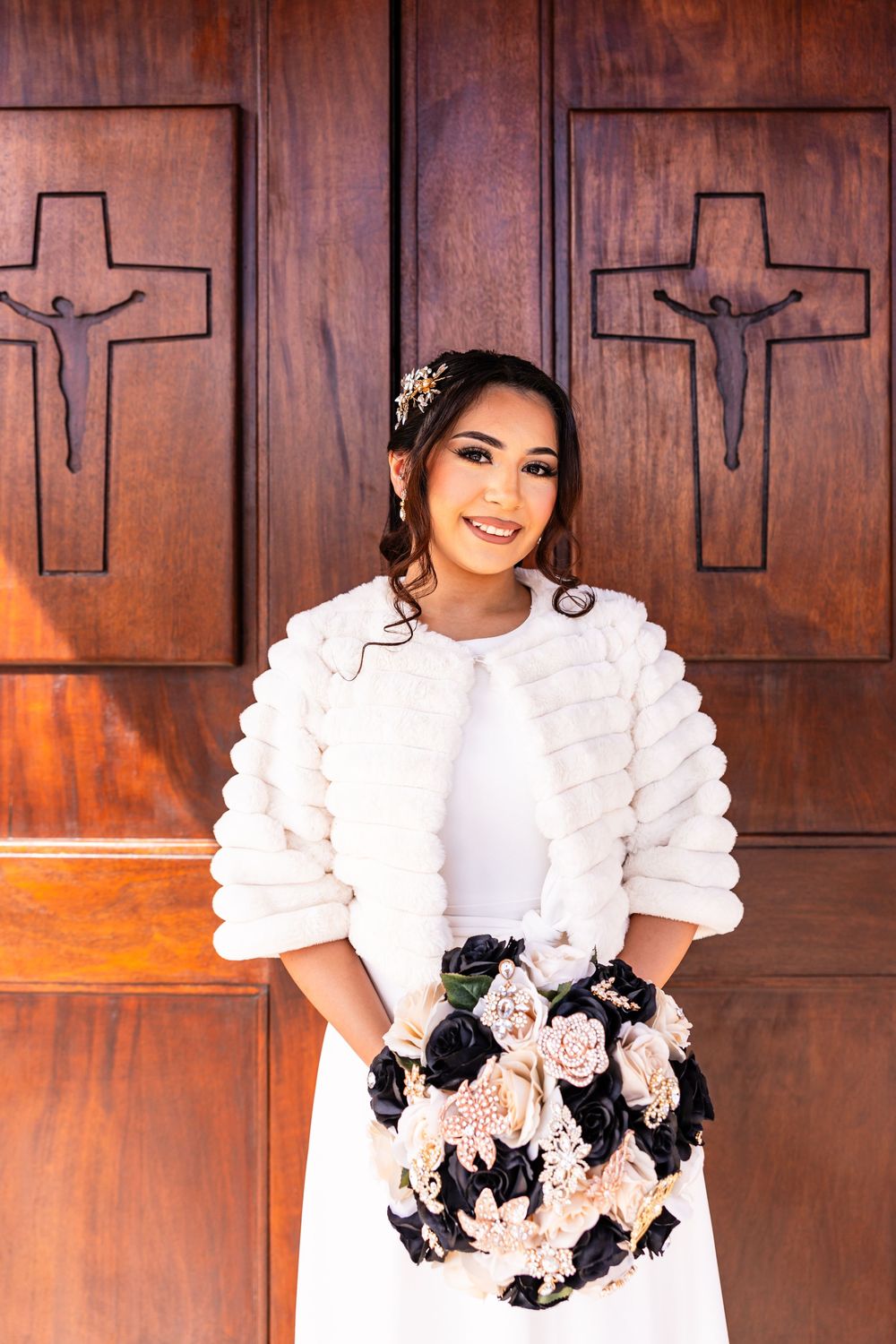 A woman in a white ruffled dress with black and pink floral accents poses against a wooden paneled wall.