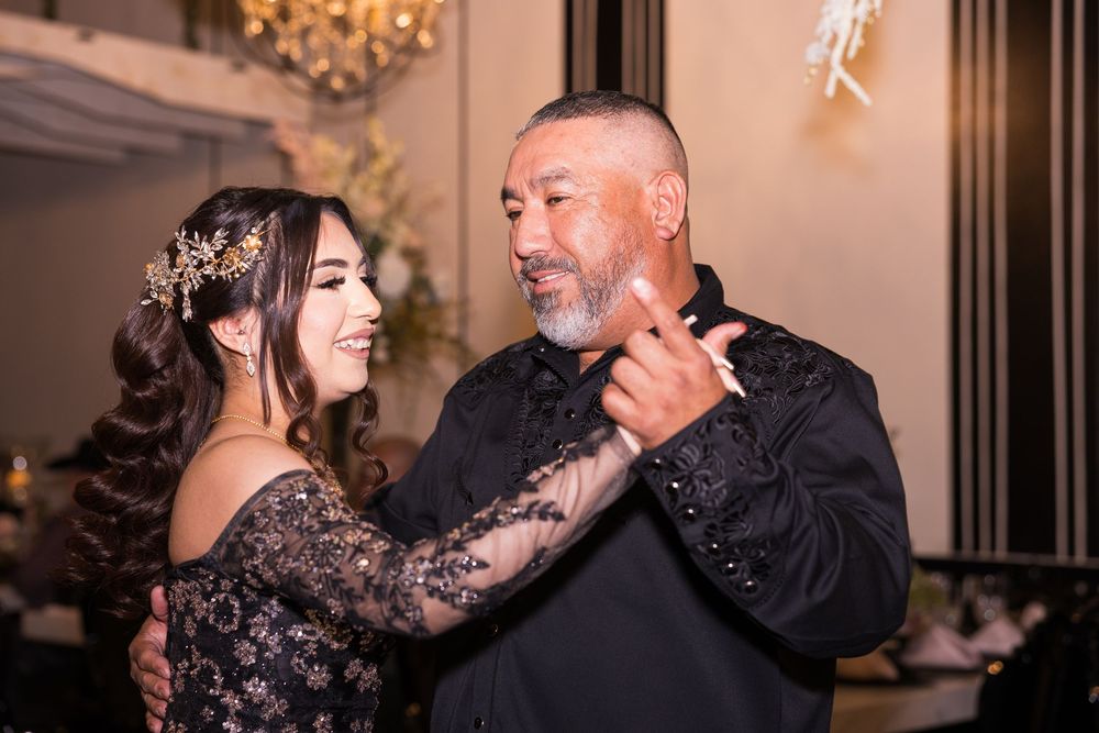 Couple in formal attire dancing together at an elegant venue with a chandelier in the background.